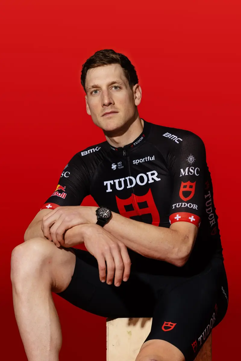 Stefan Küng sitzend im Tudor-Trikot vor rotem Hintergrund